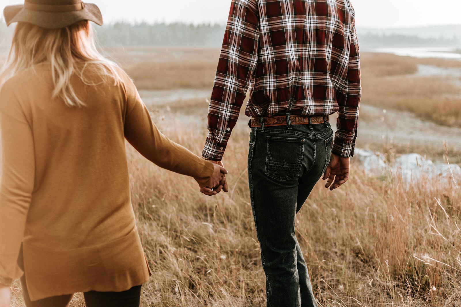 man and woman walking along grass field while holding hands